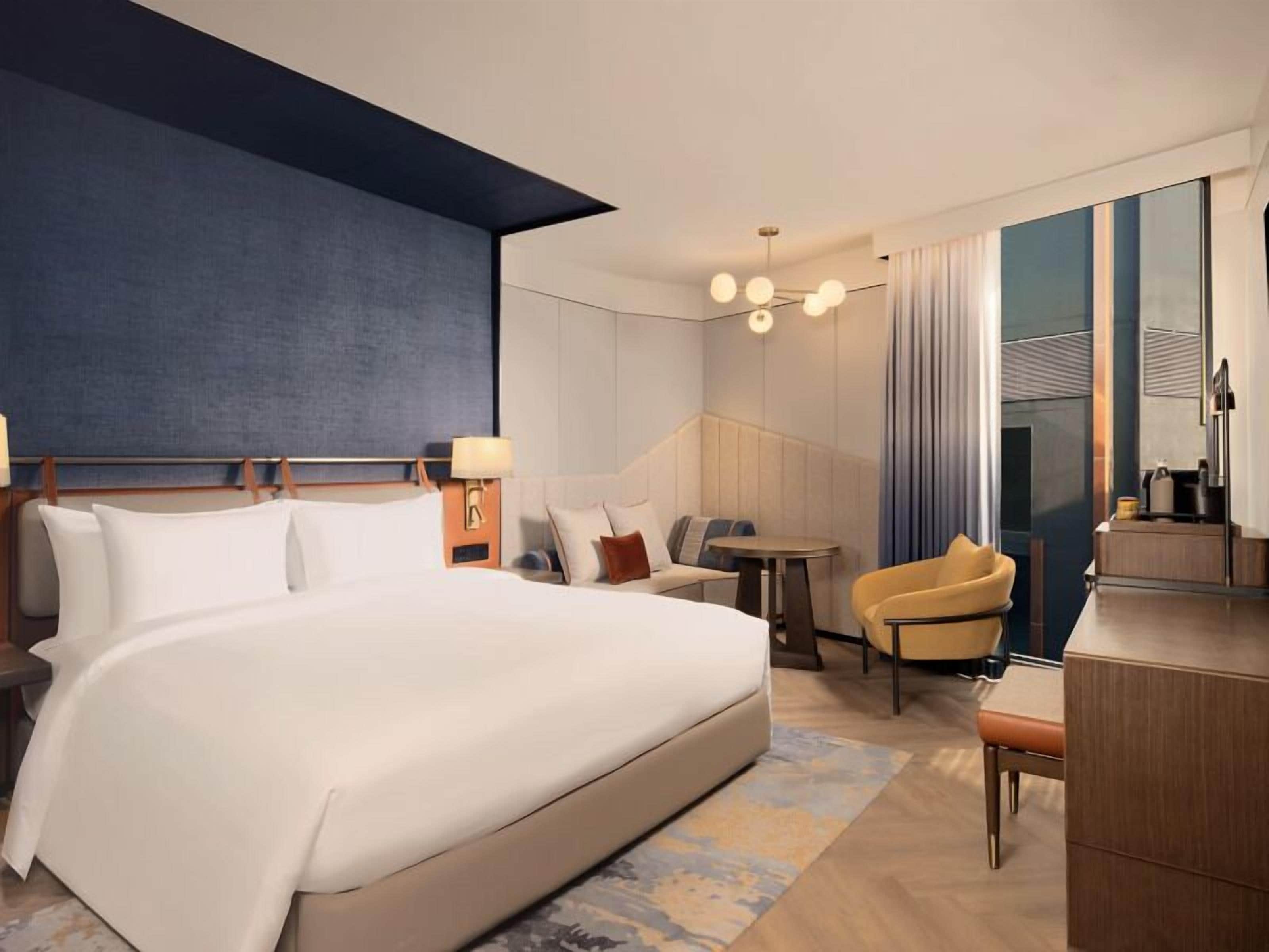 Una habitación de hotel moderna con una cama grande, una zona de estar con una mesa y un escritorio.
