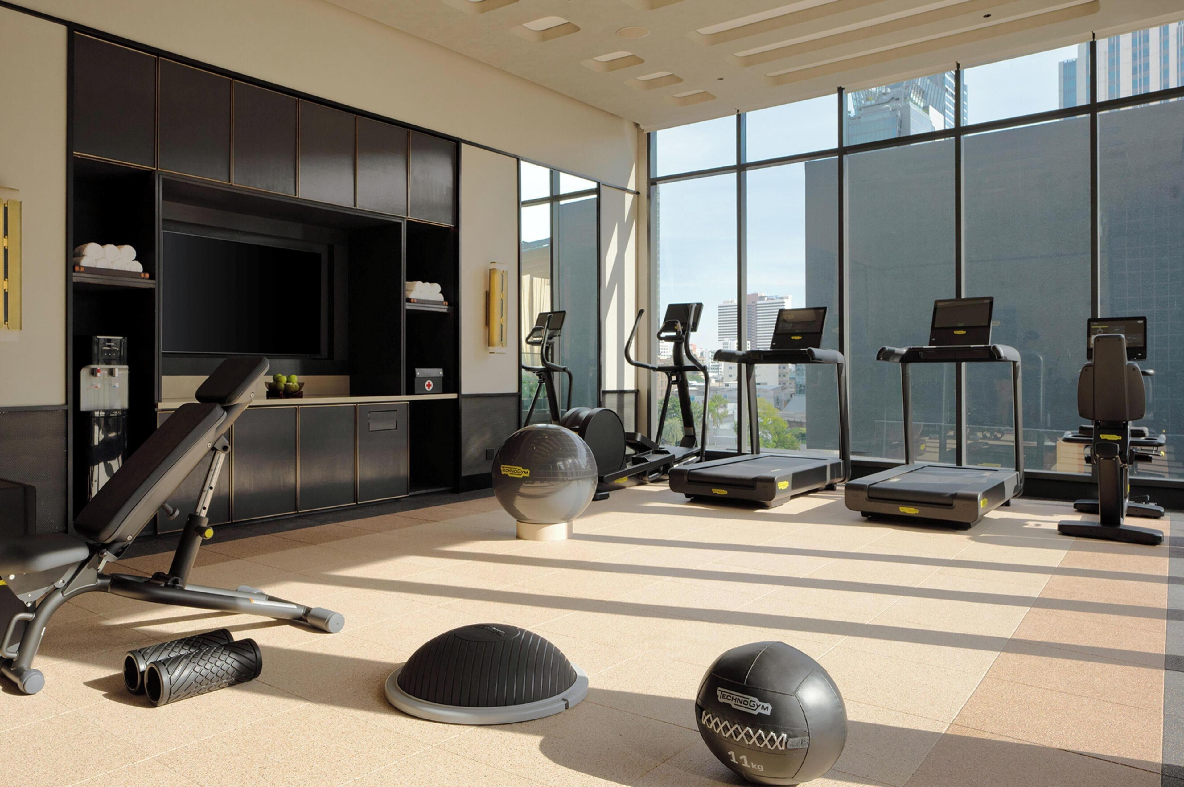 A modern gym with exercise equipment, a television, and large windows.