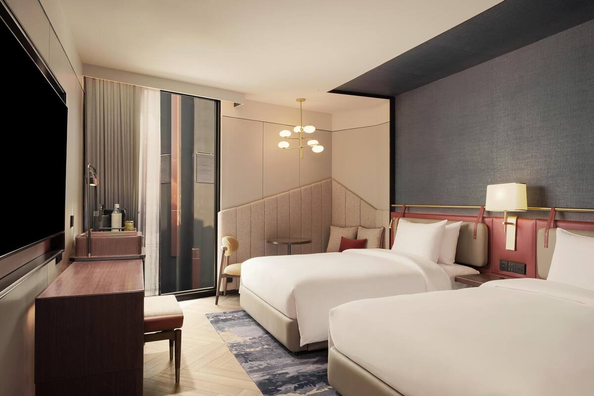 Una habitación de hotel moderna con dos camas, un escritorio, una silla, un televisor y una mesita.