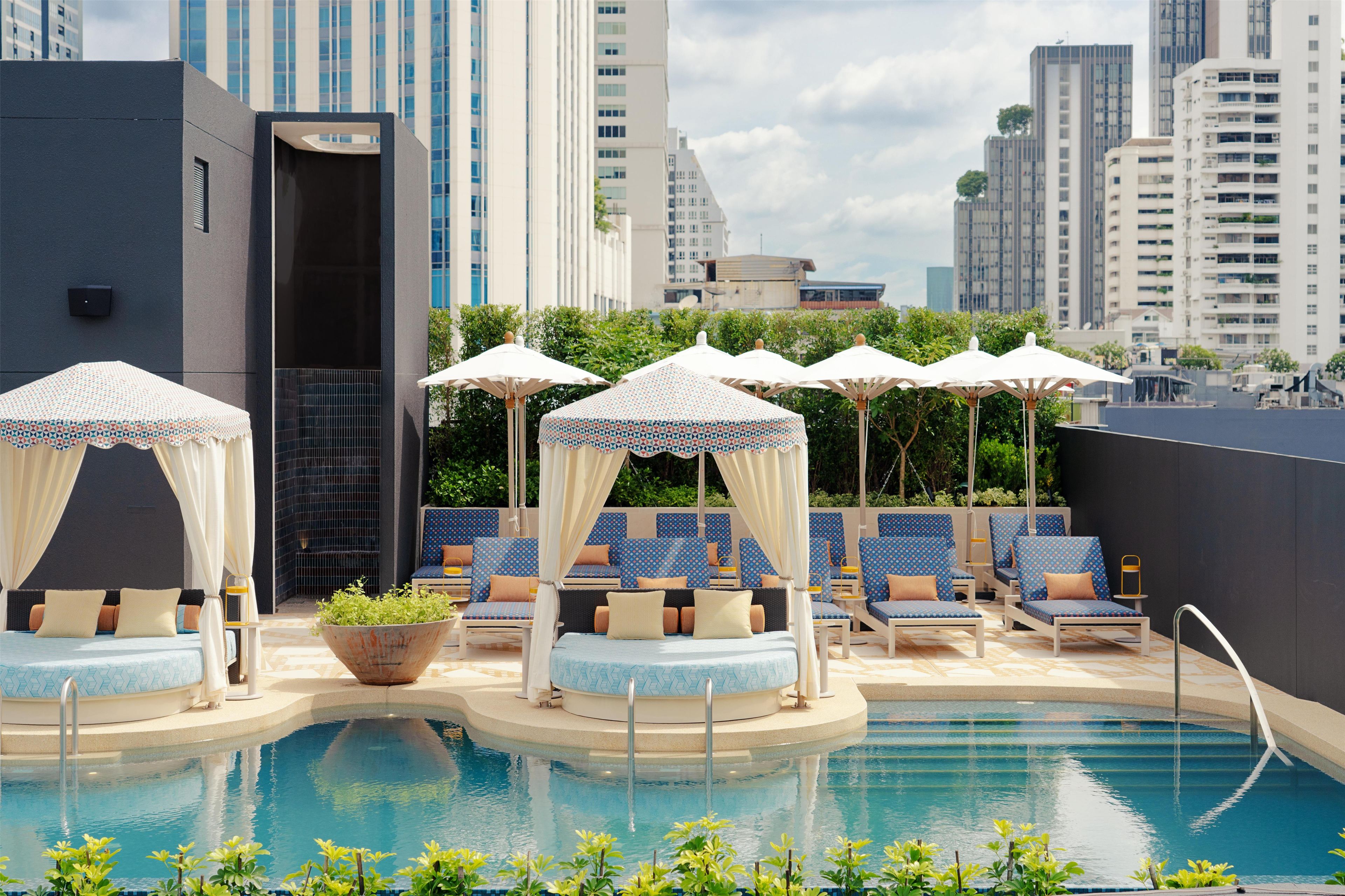 A rooftop pool area with a bed, lounge chairs, and umbrellas.