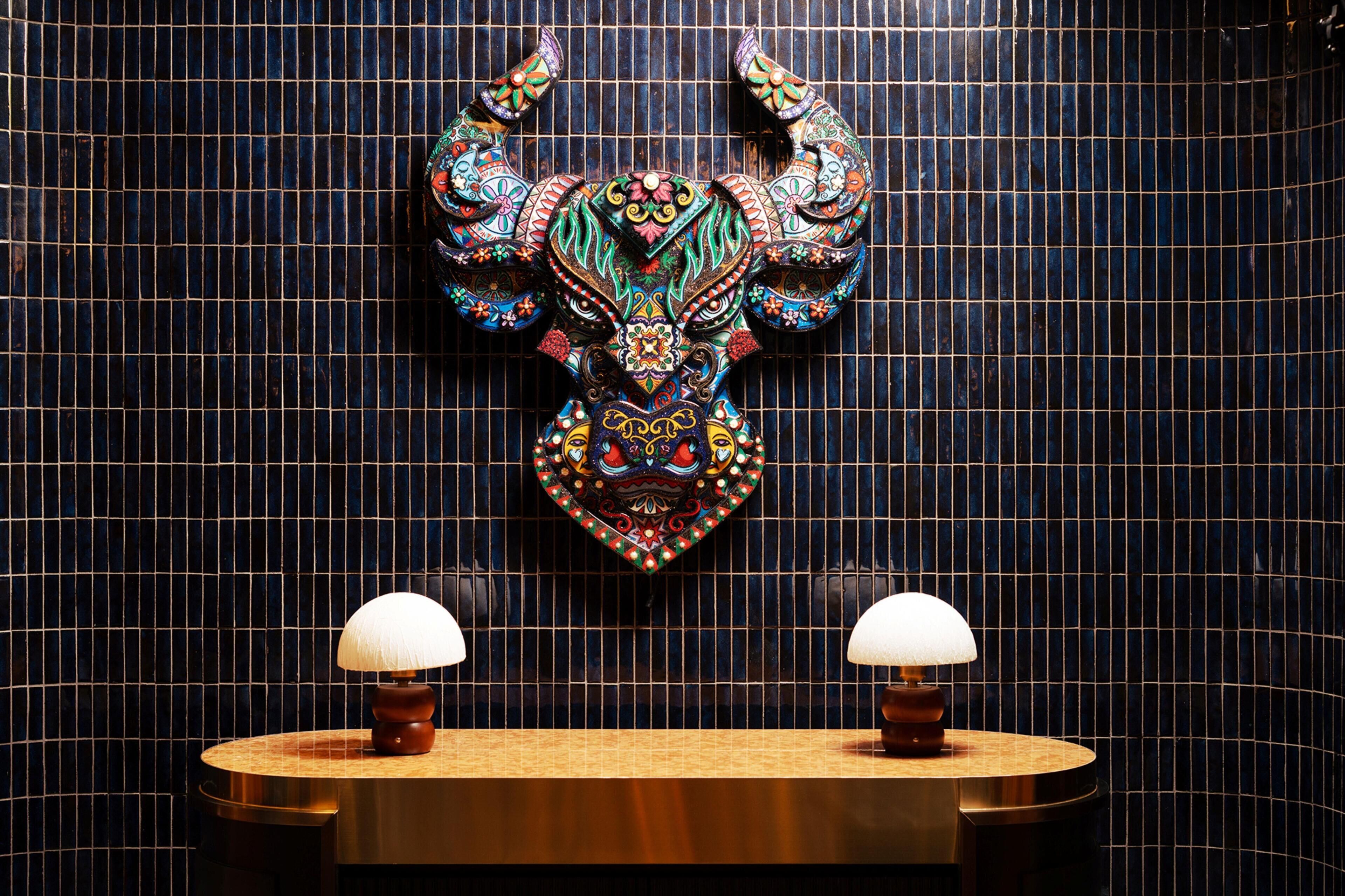 Ein Badezimmer mit einer dekorativen Wandskulptur und zwei runden Tischen mit Lampen.