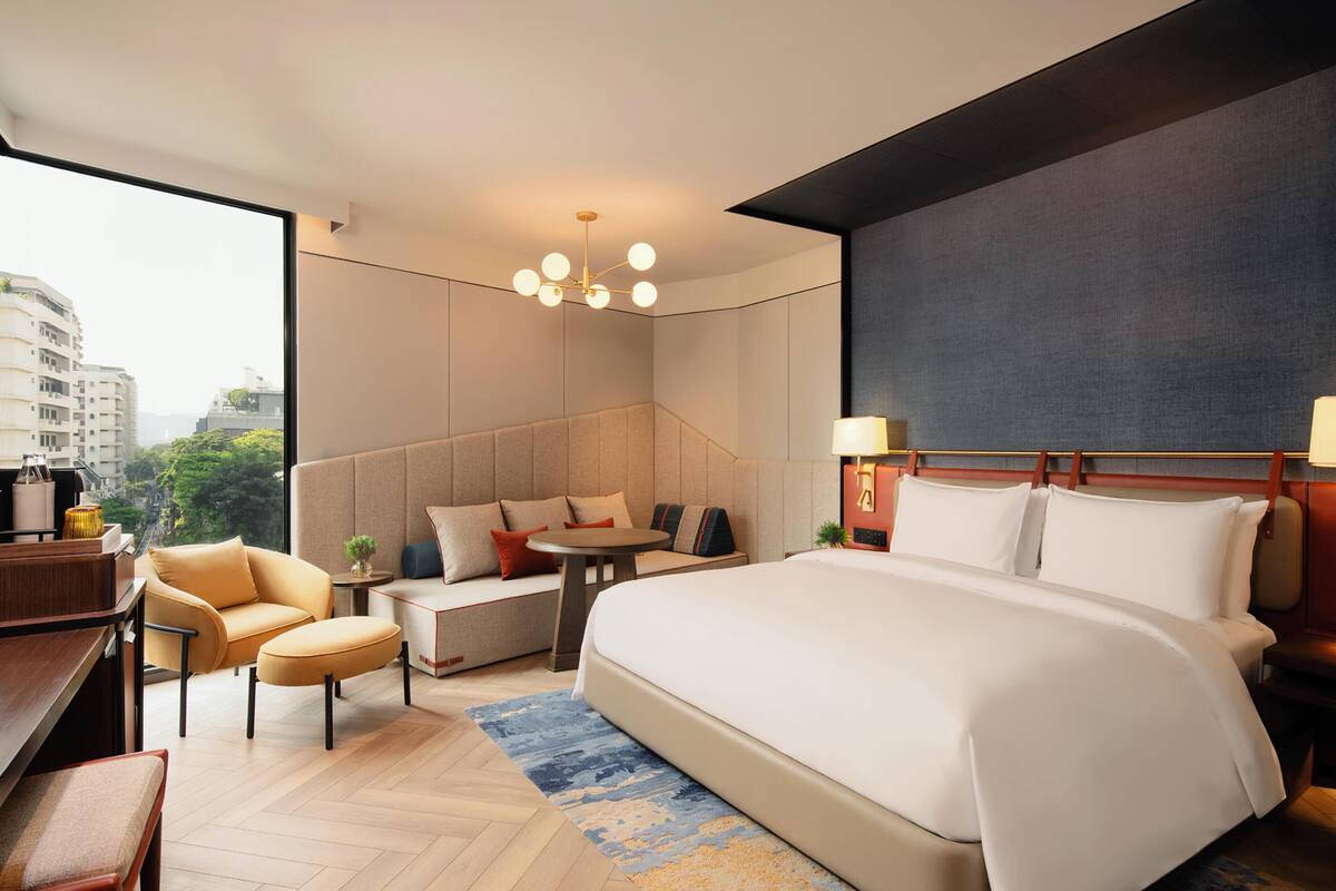 Una habitación de hotel moderna con una cama grande, un área de estar con un sofá y sillones, una mesita y vistas a la ciudad.