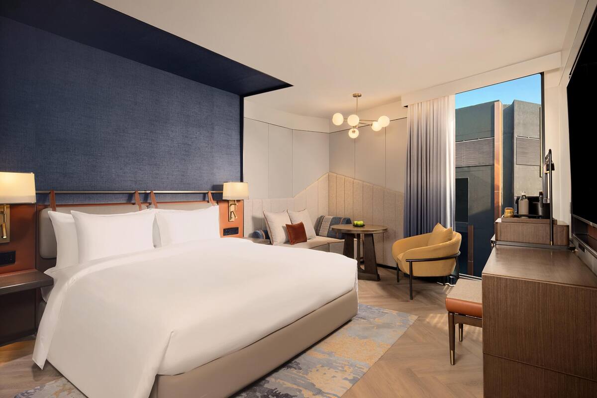 Habitación de hotel con una cama grande, un escritorio, una silla, un televisor y vistas a la ciudad.