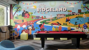 A pool table in a room with a mural depicting various activities and a sign that reads 'RIDGELAND'.