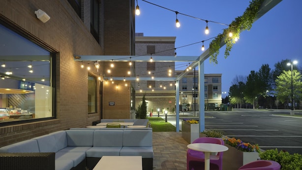 An outdoor seating area with a sofa, tables, and chairs, under a covered section with string lights. - Tru By Hilton Ridgeland Jackson (Ridgeland)