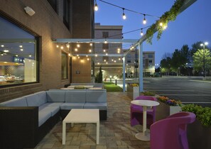 An outdoor seating area with a sofa, tables, and chairs, under a covered section with string lights. - Tru By Hilton Ridgeland Jackson (Ridgeland)