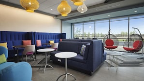 A modern lounge area with sofas, chairs, and hanging chairs, featuring large windows and ceiling lights. - Tru By Hilton Ridgeland Jackson (Ridgeland)
