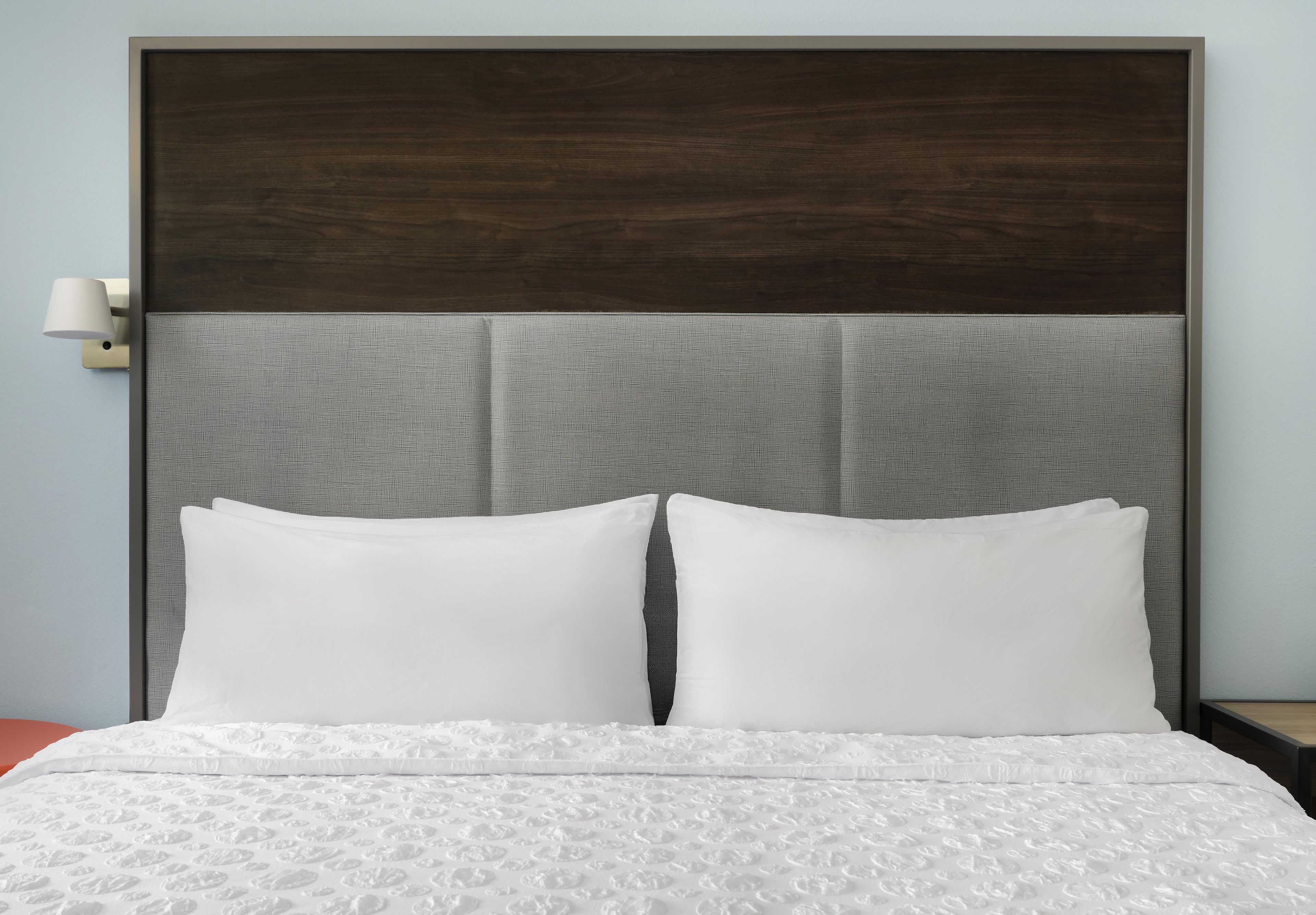 A bed with white bedding and a headboard with a textured grey panel.