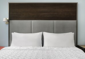 Una cama con ropa blanca y un cabecero con un panel gris texturizado.