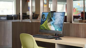A workspace with a computer monitor displaying a scenic wallpaper, a keyboard, and a green chair.