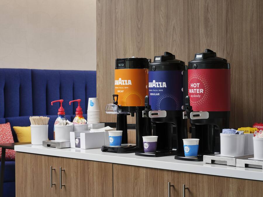 Una camera d'albergo con un angolo caffè dotato di tre erogatori, un divano e un tavolo con tazze e condimenti.