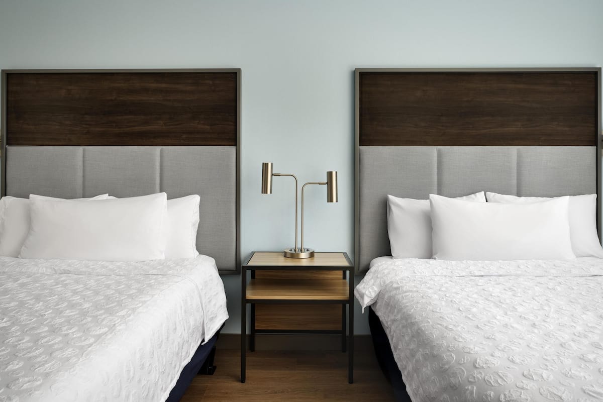 A hotel room with two beds, a nightstand, and a lamp.