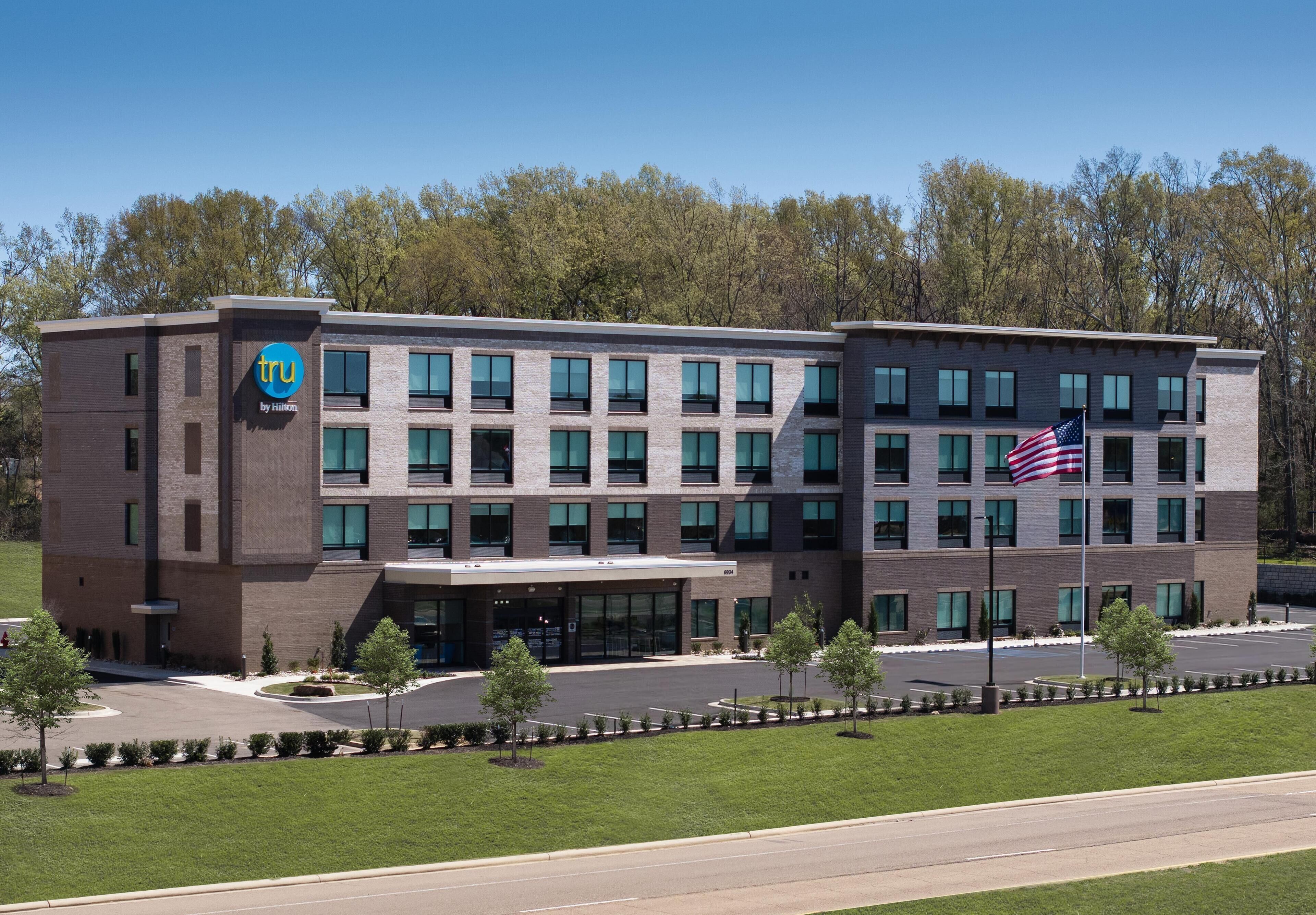 A multi-story hotel with a prominent 'tru' logo, a flag, and a landscaped entrance.