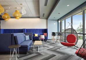 A modern lounge area with a blue sofa, a small table, hanging chairs, and a large window providing a view.