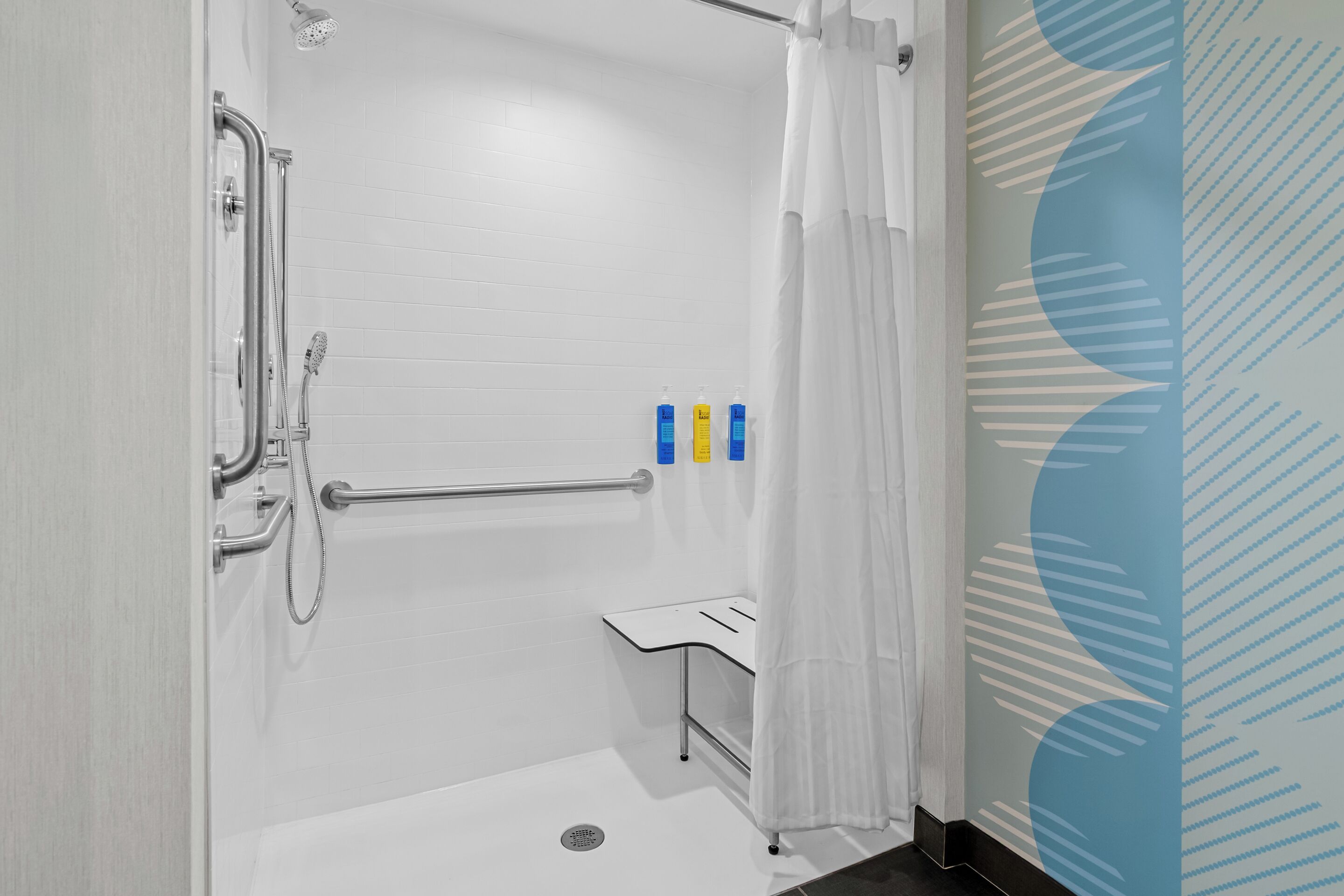 A modern bathroom with a walk-in shower, grab bars, and a hand sanitizer dispenser.