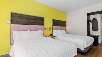 A hotel room with two beds, a wooden headboard, a bedside table with a lamp, and a coat rack.