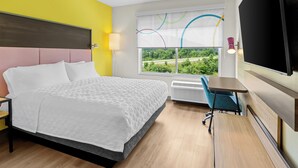 Ein Hotelzimmer mit Bett, Schreibtisch, Stuhl, Fernseher und einem Fenster mit Blick auf Grünfläche.