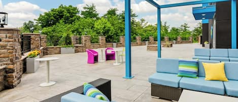 An outdoor patio area with seating arrangements, a stone wall, and a view of greenery.
