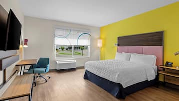 A hotel room with a bed, desk, chair, and a large window with a view of a building.