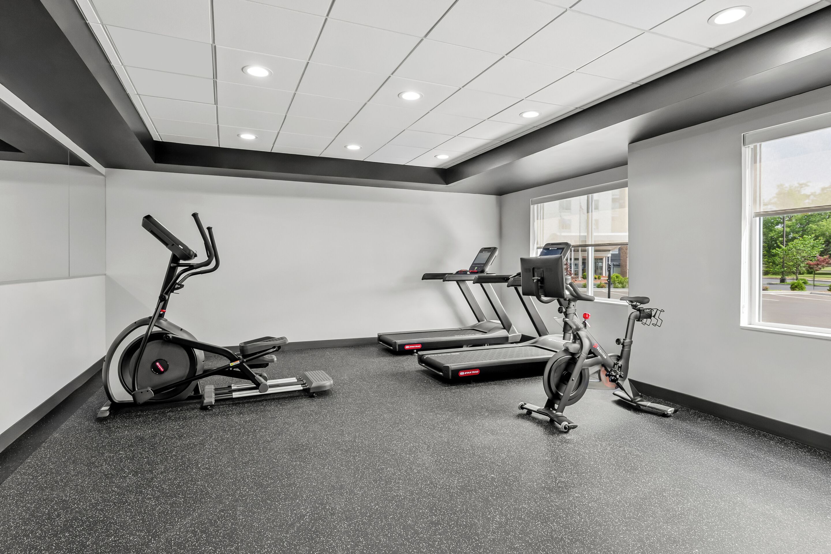 Ein Fitnessraum mit Fahrrädern und Laufbändern, einem großen Fenster und einer Decke mit Einbaustrahlern.