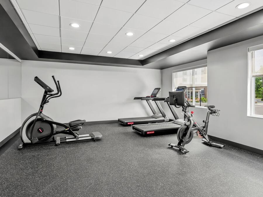 A gym with stationary bikes and treadmills, a large window, and a ceiling with recessed lighting.