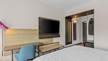 Ein modernes Hotelzimmer mit Bett, Schreibtisch, Stuhl, Wandfernseher und Spiegel.