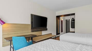 Habitación de hotel con cama, escritorio, silla, televisión y baño con espejo y toallero.