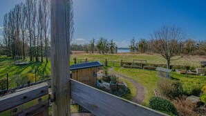 Een houten terras met uitzicht op een grasveld, een klein houten gebouwtje en een waterpartij in de verte.
