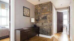 Une chambre moderne avec un mur d’accent en pierre, un plancher en bois, un lit avec une literie à motifs, une commode en bois foncé et une œuvre d’art encadrée accrochée au mur.