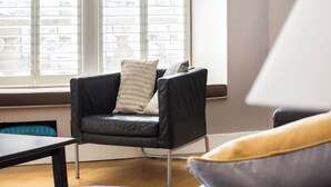 Un salon moderne avec un fauteuil en cuir noir, une table en bois et un canapé agrémenté de coussins.