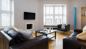 Un salon moderne avec un canapé en cuir noir, une table basse et un téléviseur fixé au mur.