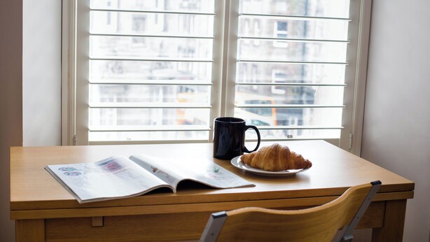 Une table en bois avec un magazine, une tasse noire et une assiette contenant un croissant.