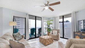 A spacious living room with a sofa, armchair, and ottoman, a ceiling fan, and a large window with blinds. - Seaside Beach & Racquet 5914 (Orange Beach)