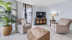 A living room with a sofa, armchair, and ottoman, a television, a cabinet, and a large potted plant. - Seaside Beach & Racquet 5914 (Orange Beach)
