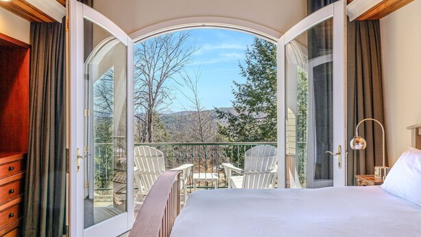 A bedroom with a large bed, a balcony with chairs, and a view of trees and hills. - Retreat w/ Southern Views | Hot Tub | Club Access (Hartford)
