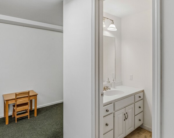 A bathroom with a white sink, mirror, and cabinet, a wooden chair, and a carpeted floor. - Retreat w/ Southern Views | Hot Tub | Club Access (Hartford)