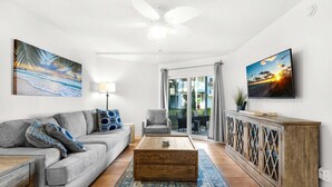 A living room with a grey sofa, a wooden coffee table, a cabinet with glass doors, and a ceiling fan. - Sand Dollar E-101 (Pensacola Beach)