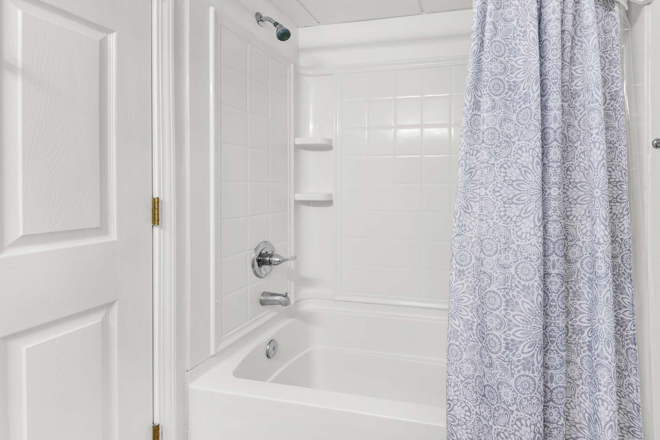 A bathroom with a white bathtub, a shower, and a patterned curtain.