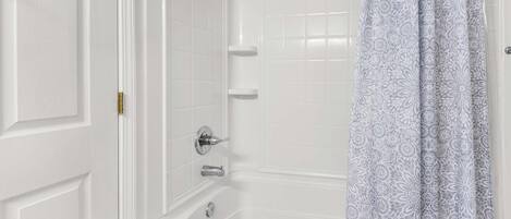A bathroom with a white bathtub, a shower, and a patterned curtain.