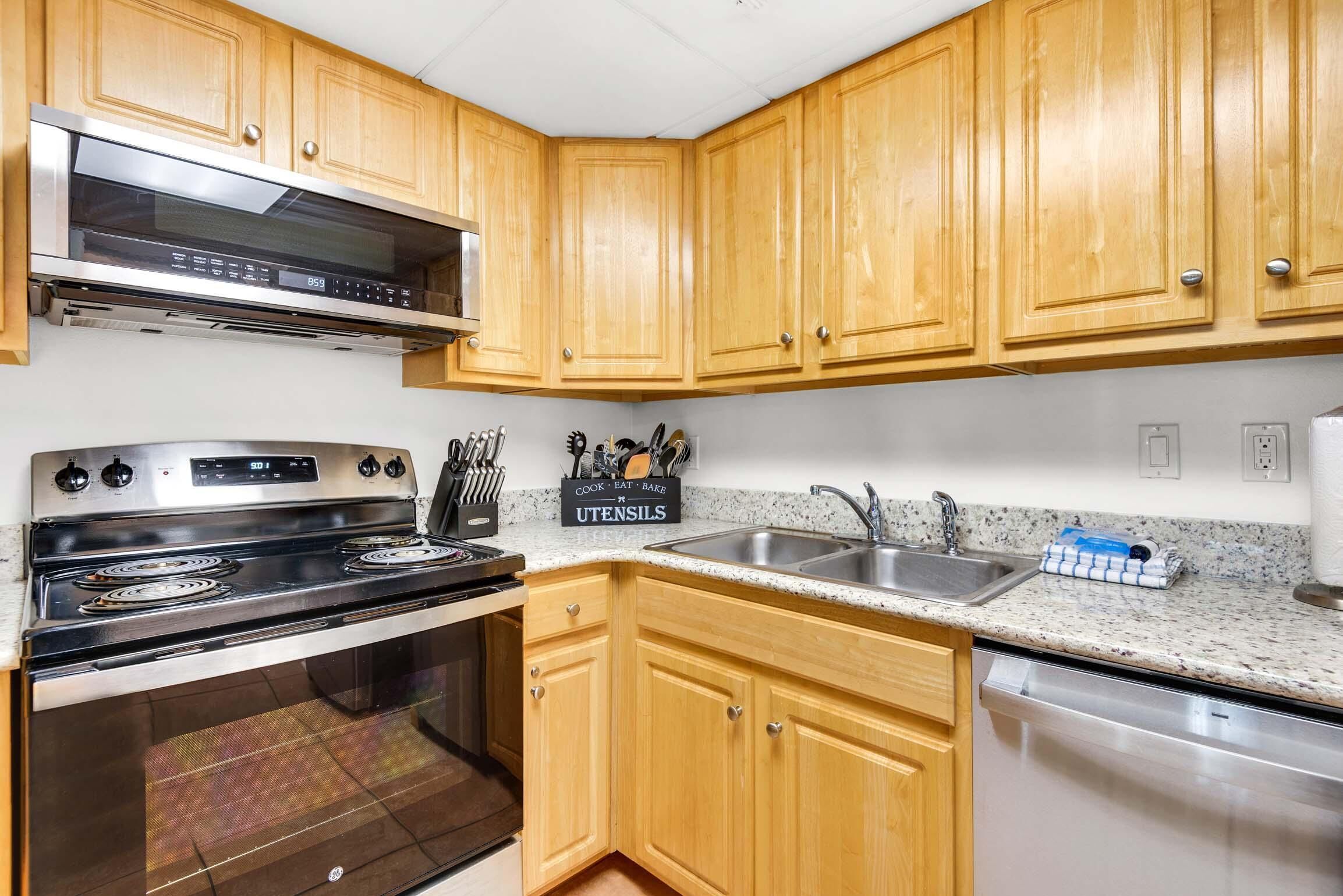 A kitchen with wooden cabinets, stainless steel appliances, a granite countertop, and a dish rack.