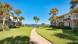 A pathway leading to a beachfront hotel with palm trees and a clear view of the ocean. - Sand Dollar E-101 (Pensacola Beach)