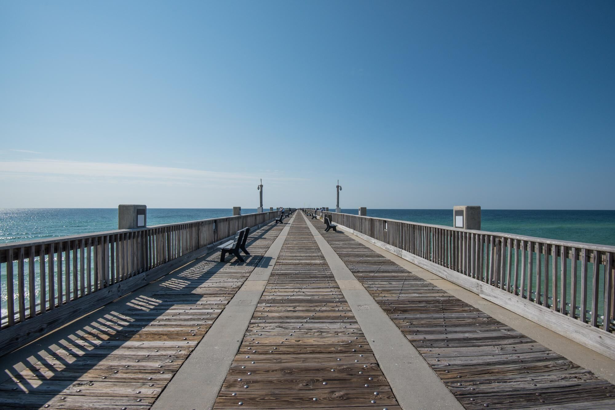 A wooden pier extending into the ocean with benches and a clear sky.