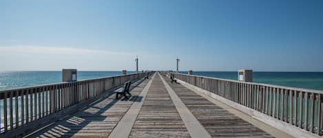 A wooden pier extending into the ocean with benches and a clear sky.