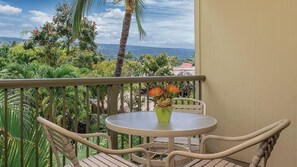 A balcony with a round table and chairs, a potted plant, and a view of the ocean and greenery. - Stunning Hawaiian Vacation: 2 Bedroom at WorldMark Kona (Kailua-Kona)