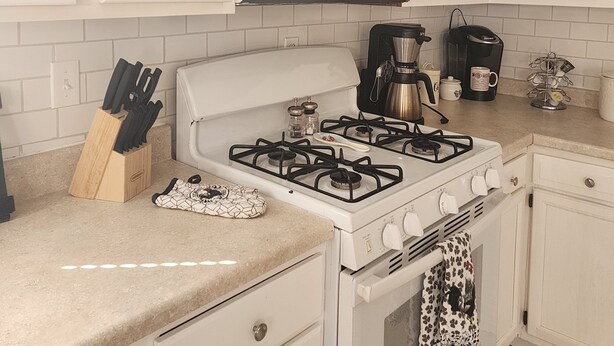 Une cuisine avec des meubles blancs, une cuisinière à gaz, un four à micro-ondes et une machine à café.