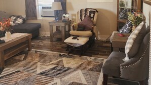 Un salon comprenant un canapé, un fauteuil, un pouf, une table basse et un tapis à motifs.