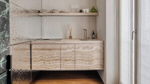 A kitchen with a marble countertop, a sink, and a shelf above it holding plates, glasses, and a vase. - Archimede by Wynwood House (Milan)
