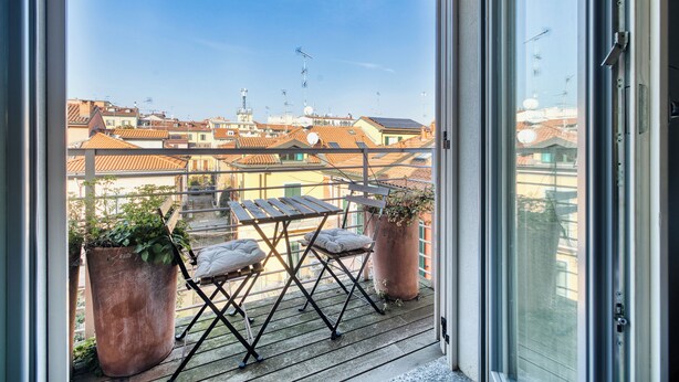 A balcony with a wooden table and two potted plants, overlooking a cityscape with red-tiled roofs. - Archimede by Wynwood House (Milan)