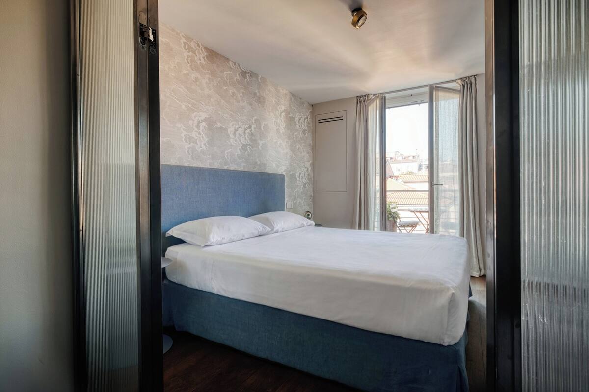 Une chambre d’hôtel avec un lit, une fenêtre avec des rideaux et une vue sur les bâtiments environnants.