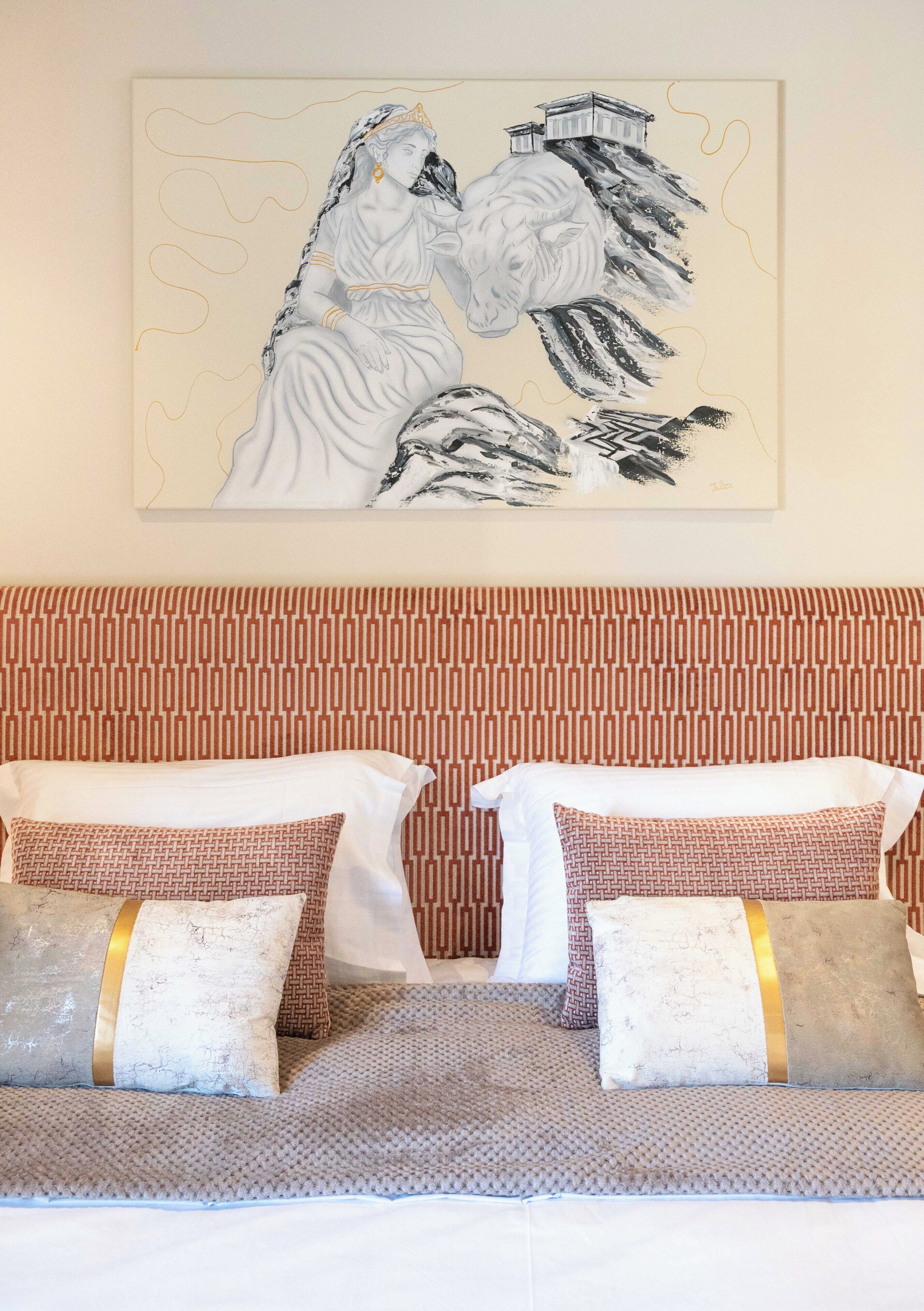 Una habitación con un cabecero estampado, un cuadro abstracto de gran tamaño y un sofá con cojines decorados.